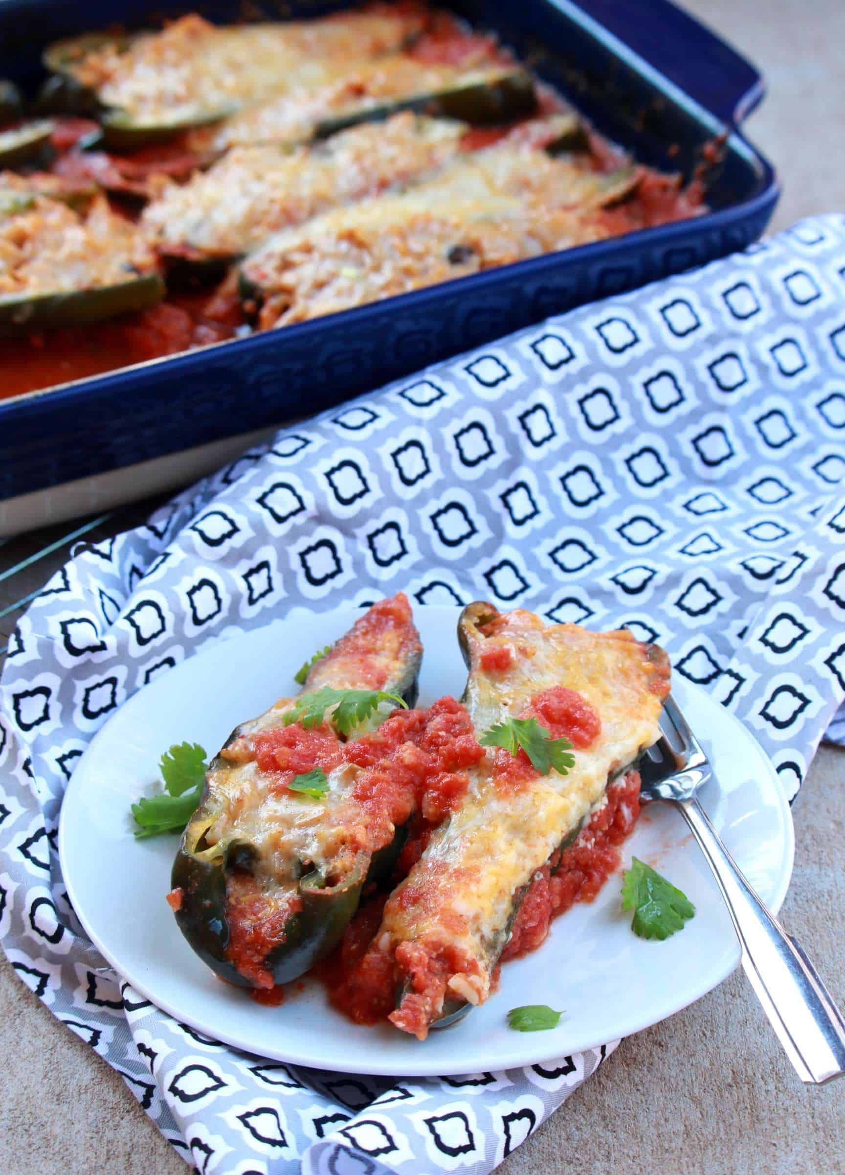 two stuffed peppers on a plate with more in a casserole