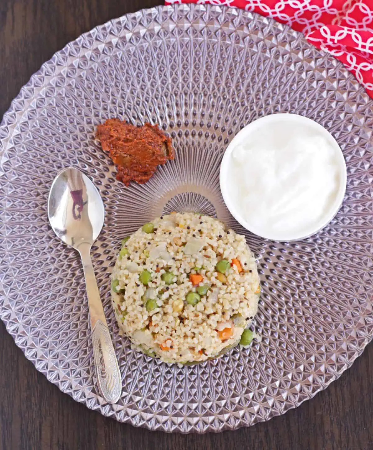 Broken wheat upma in a pink plate with pickle and yogurt and a spoon.
