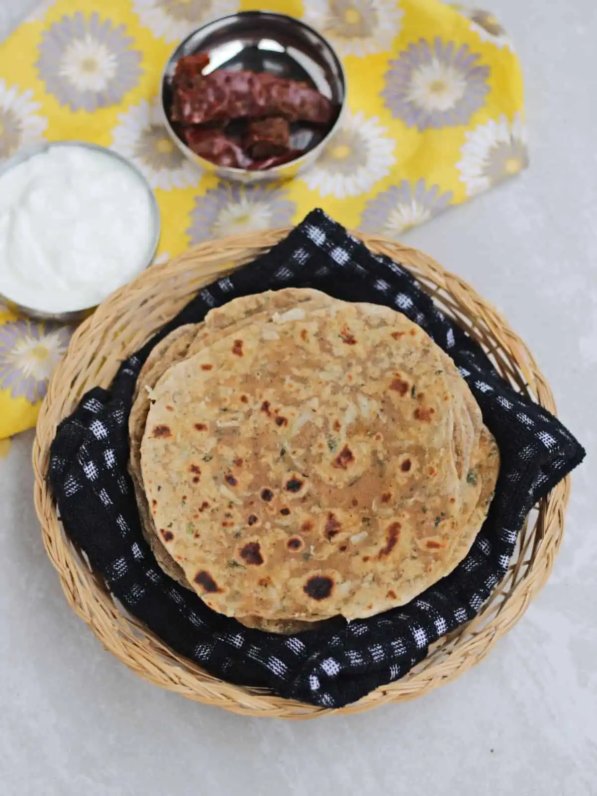 paratha layered in a basket with yogurt and pickle on the side.