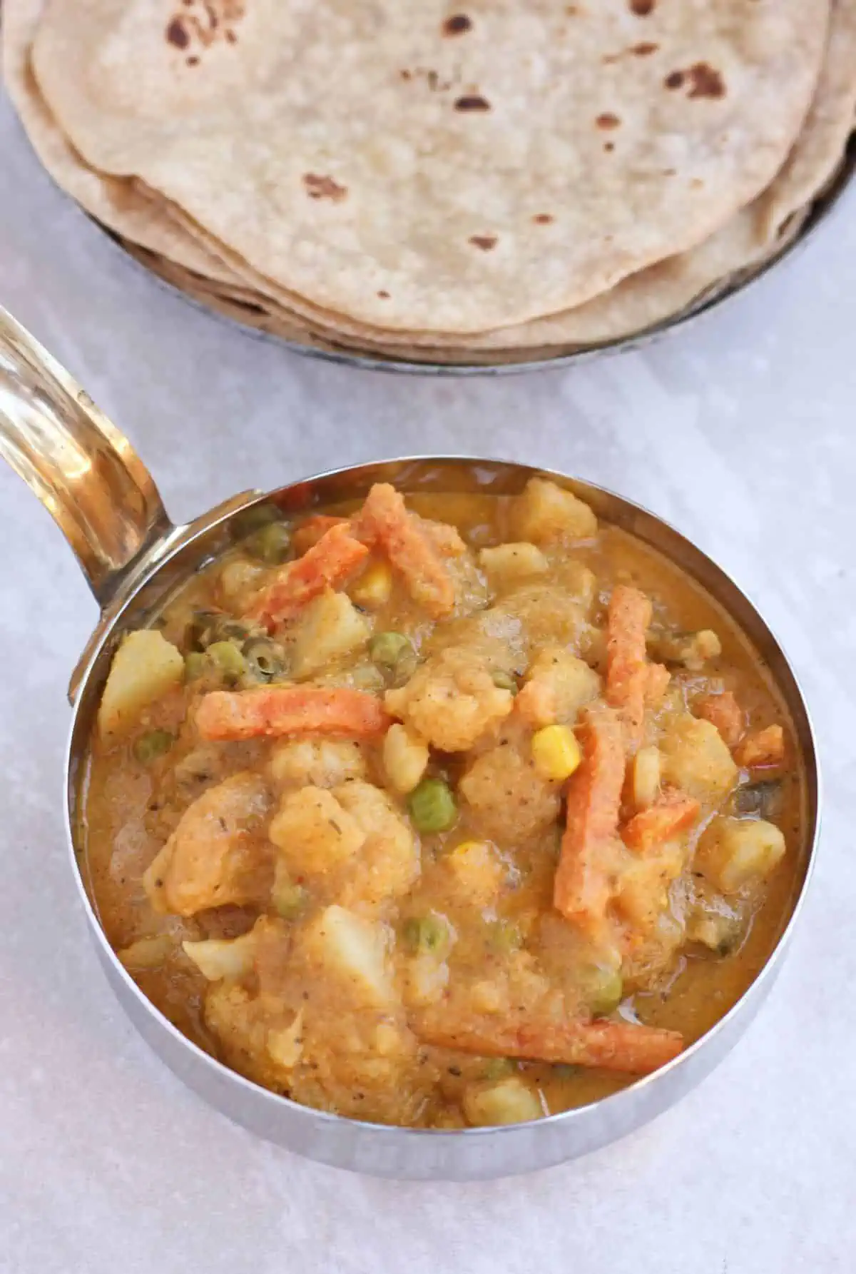 Vegetable curry in a bowl with roti in the background.