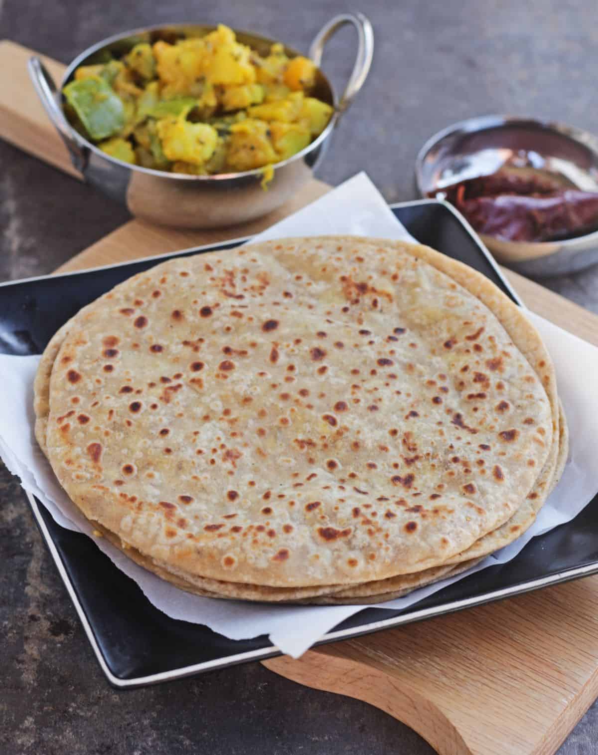 Chana dal paratha stacked in a black plate with curry and pickle.