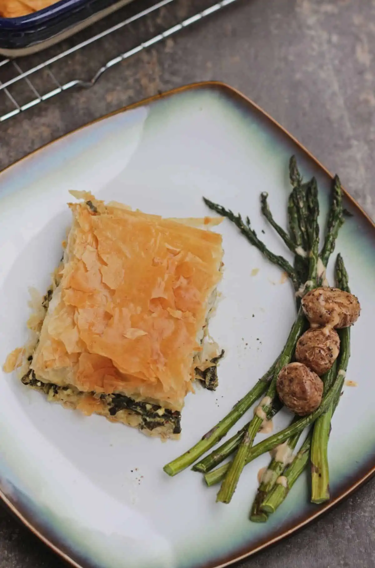 a slice of byrek mi spinaq with roasted potatoes and asparagus in a plate