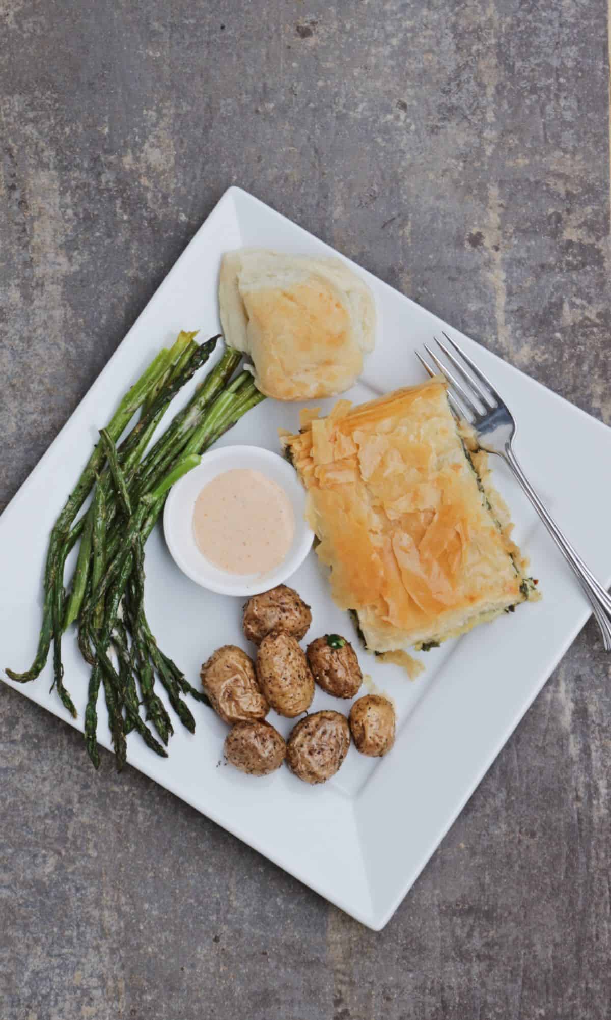 dinner plate with albanian spinach pie, roasted potatoes, asparagus, sauce and roll