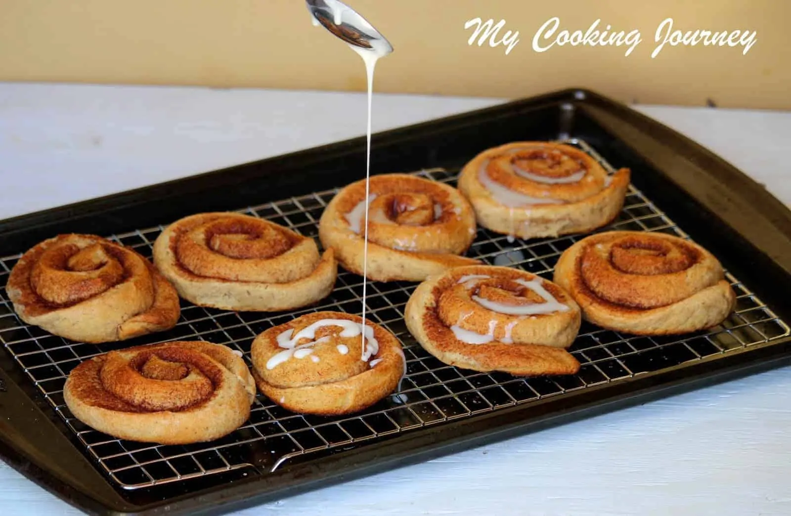 Whole Wheat Cinnamon Buns in a Wire rack and glaze pouring from spoon