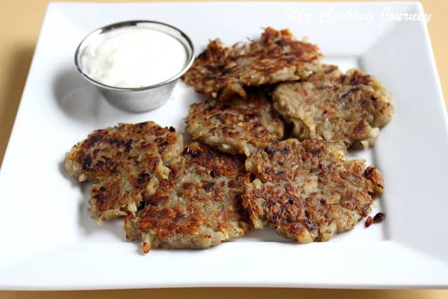 Latke stacked on a white plate with a side of sour cream.