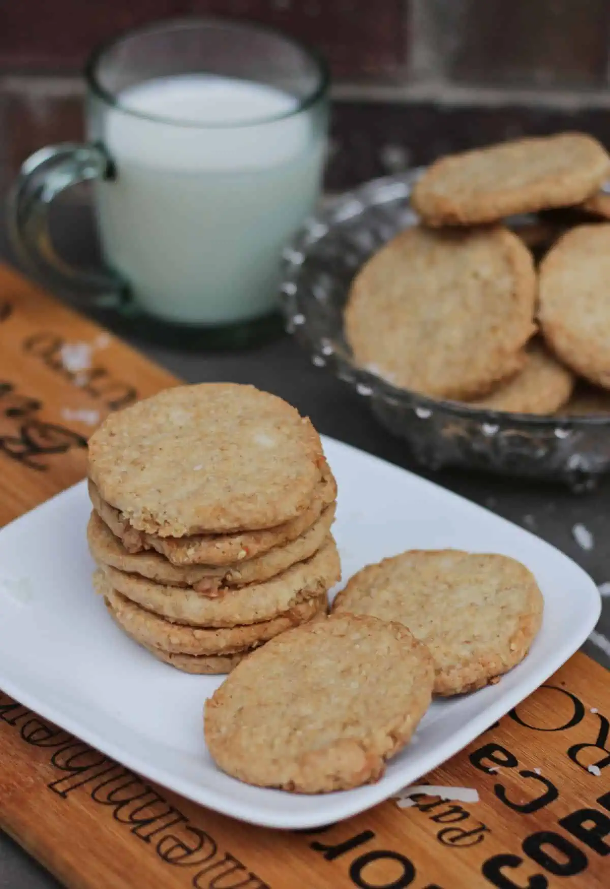coconut and sesame cookies in a plate with milk in the back. 