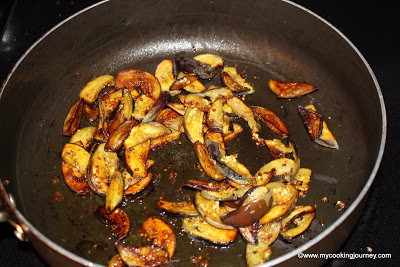 Adding eggplants to the spiced onions and frying them in a pan.
