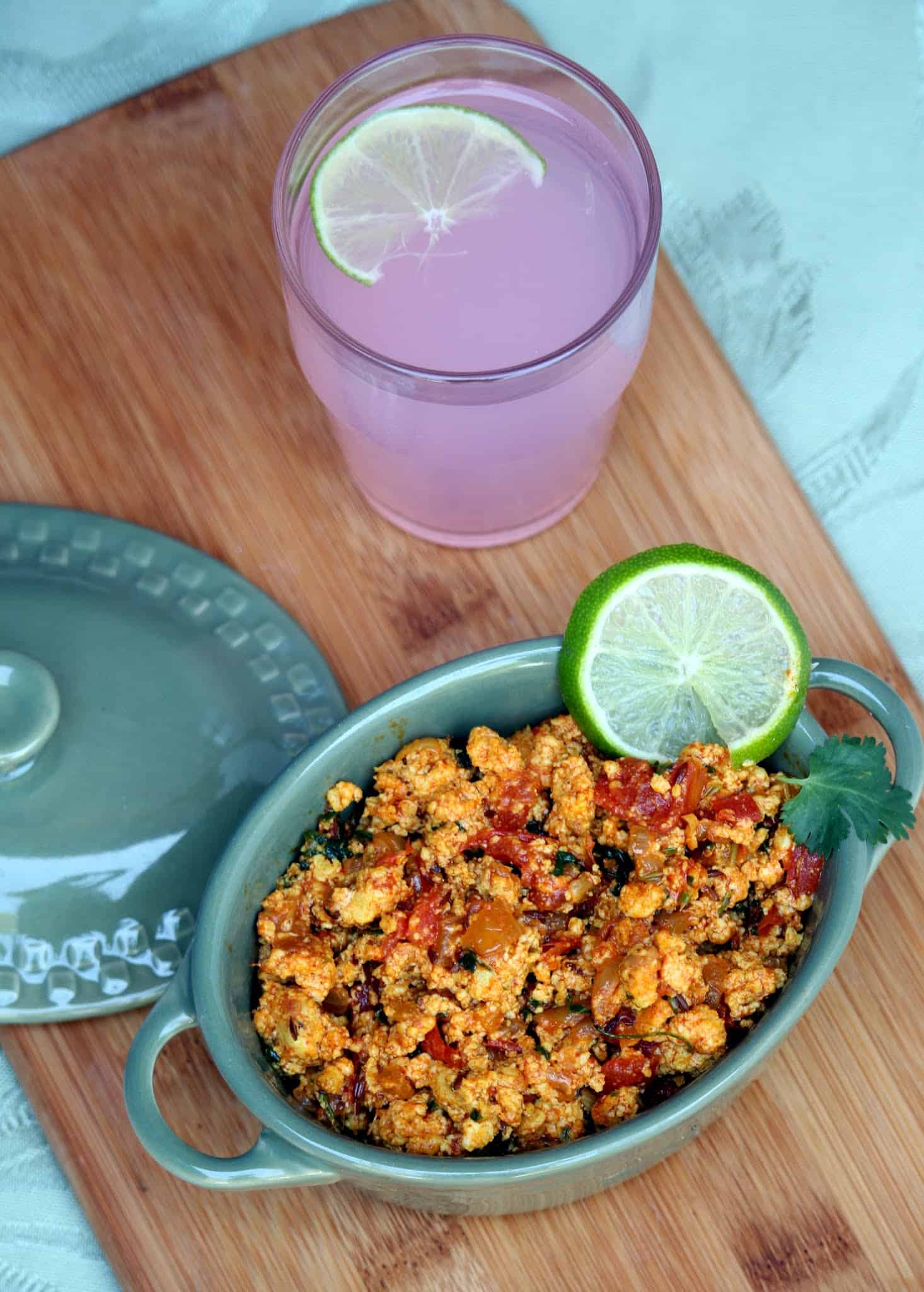 Paneer Bhurji in a green bowl with a slice of lime for garnish and pink lemonade on the side. 