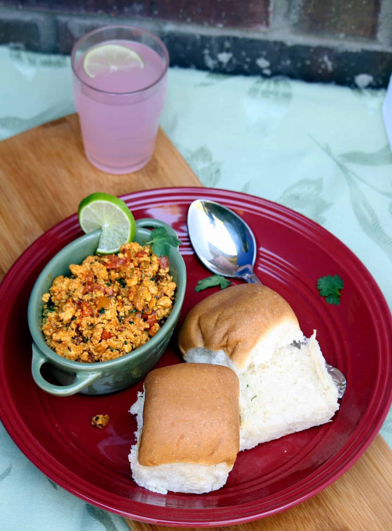 A plate of scrambled paneer bhurji served with bun and juice on the side. 