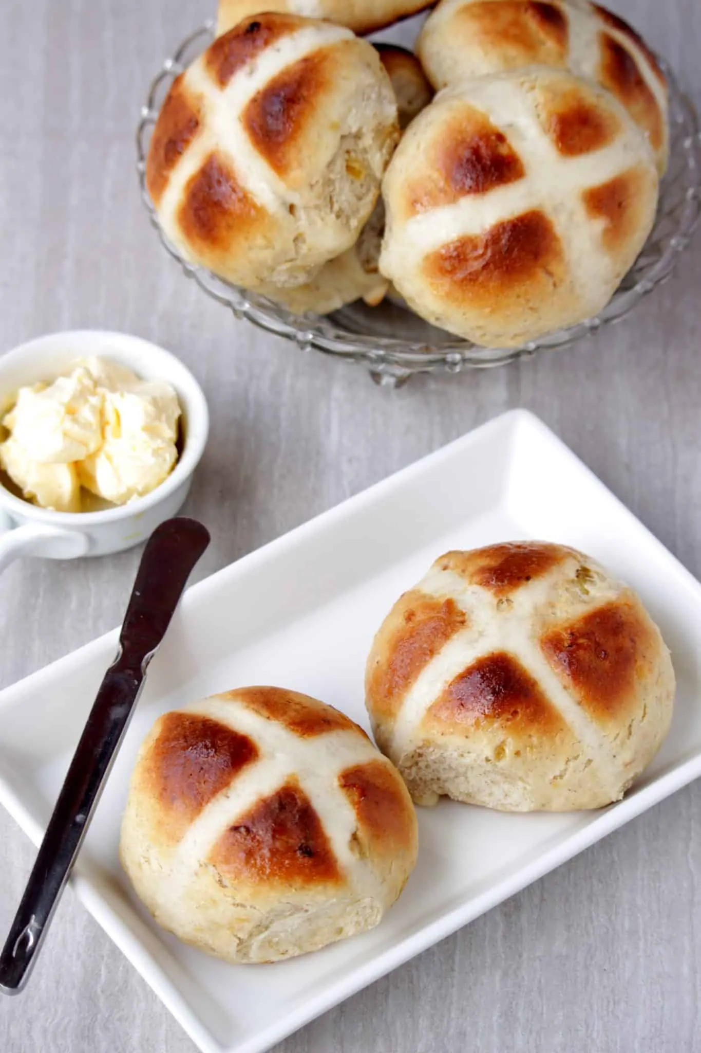 Hot Cross Buns in a white plate with butter on the side.