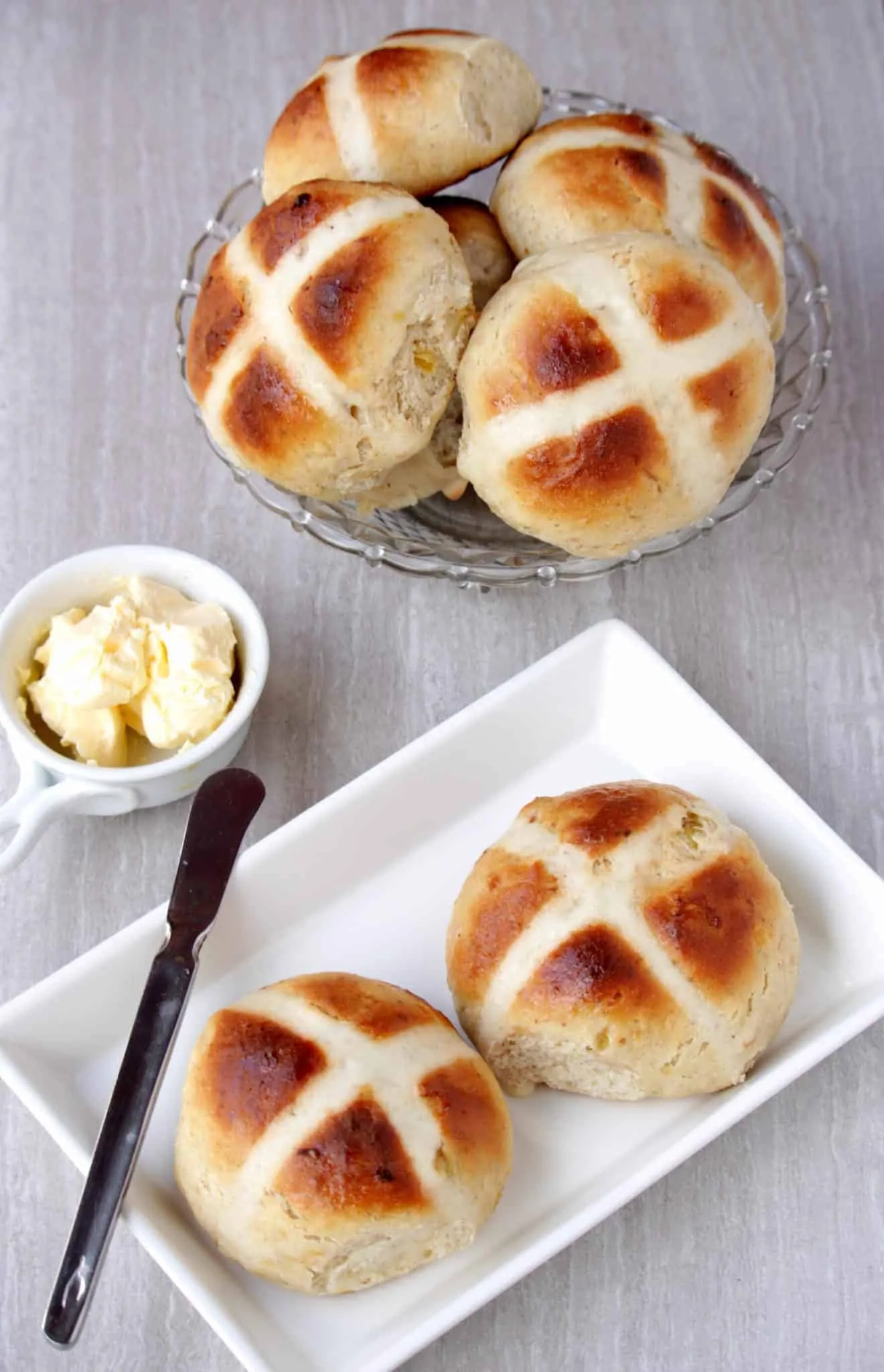 Hot Cross Buns in a white plate and glass bowl with butter on the side.