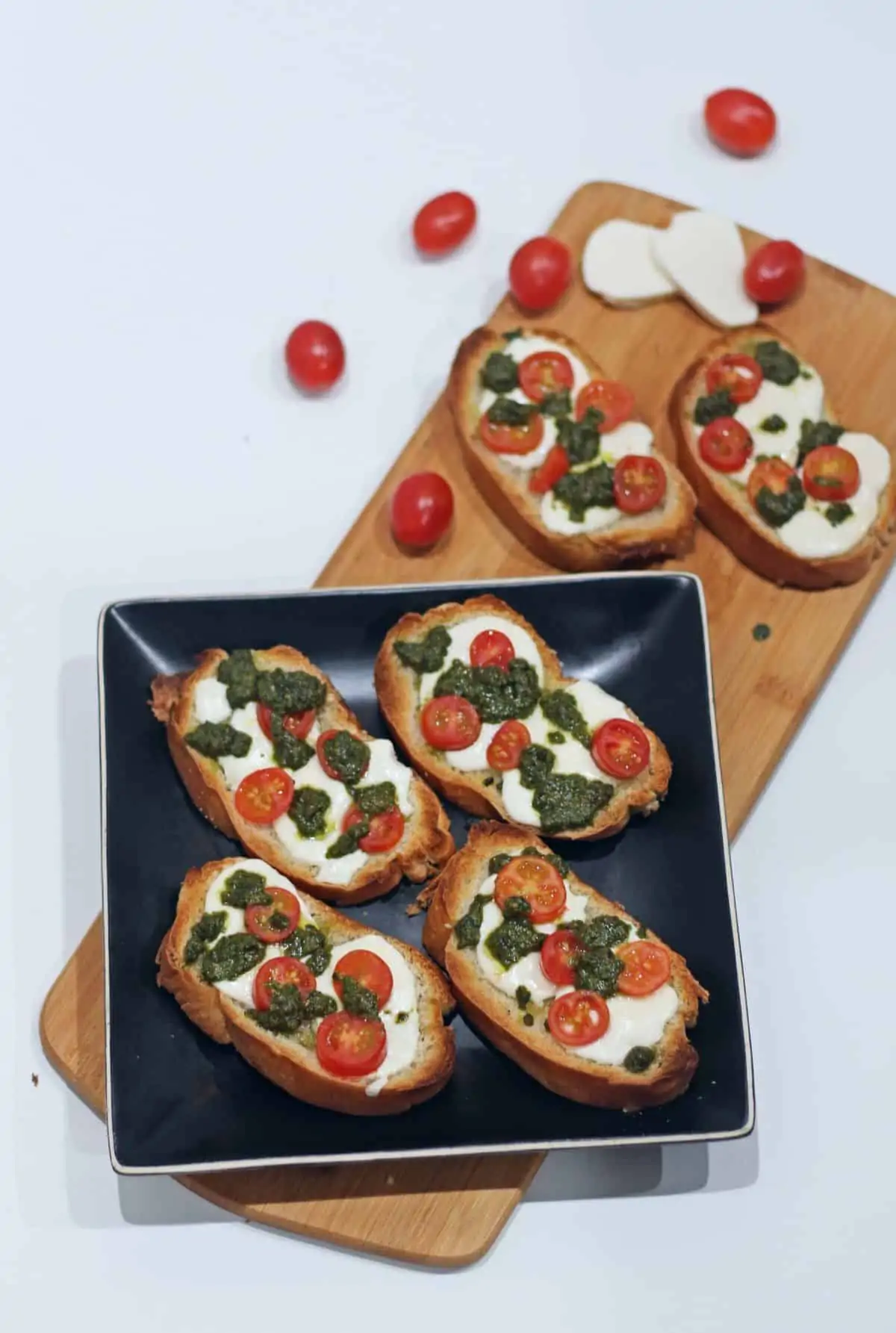 Homemade crostini with cherry tomatoes, mozzarella cheese and basil pesto on a black plate