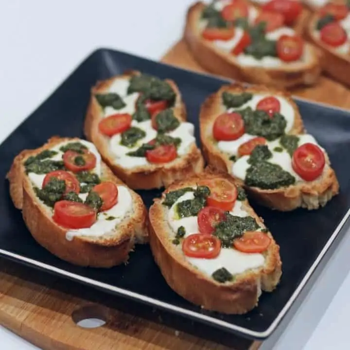 crostini with tomato, cheese and basil pesto arranged in a black plate