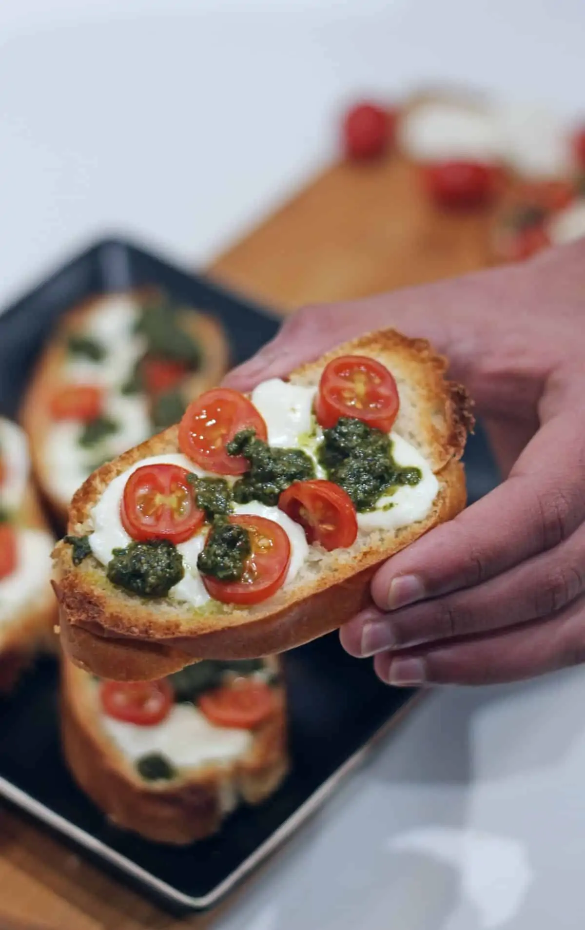 A single crostini with tomato, pesto and cheese held in hand