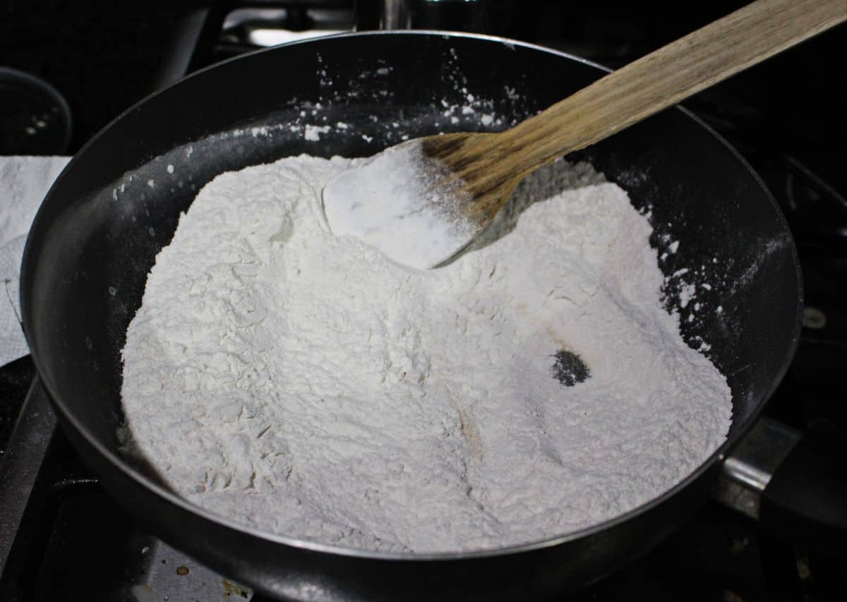 frying rice flour in a pan with a wooden ladle
