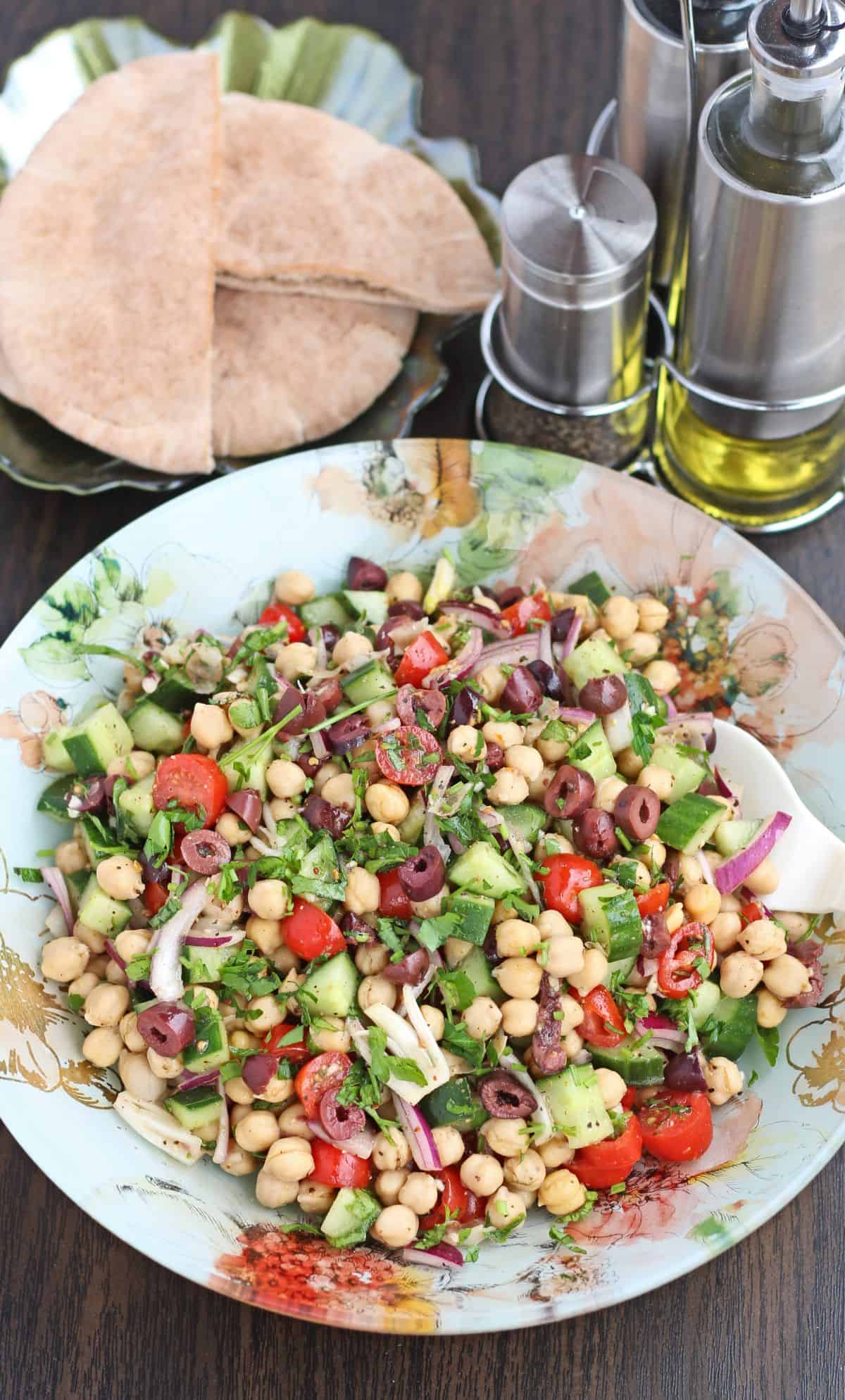 Chickpea salad in a bowl with pita bread and seasoning on side