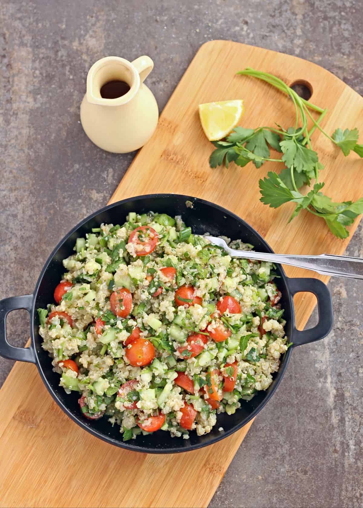 Quinoa Tabbouleh salad in a black plate with fork and parsley and dressing on the background