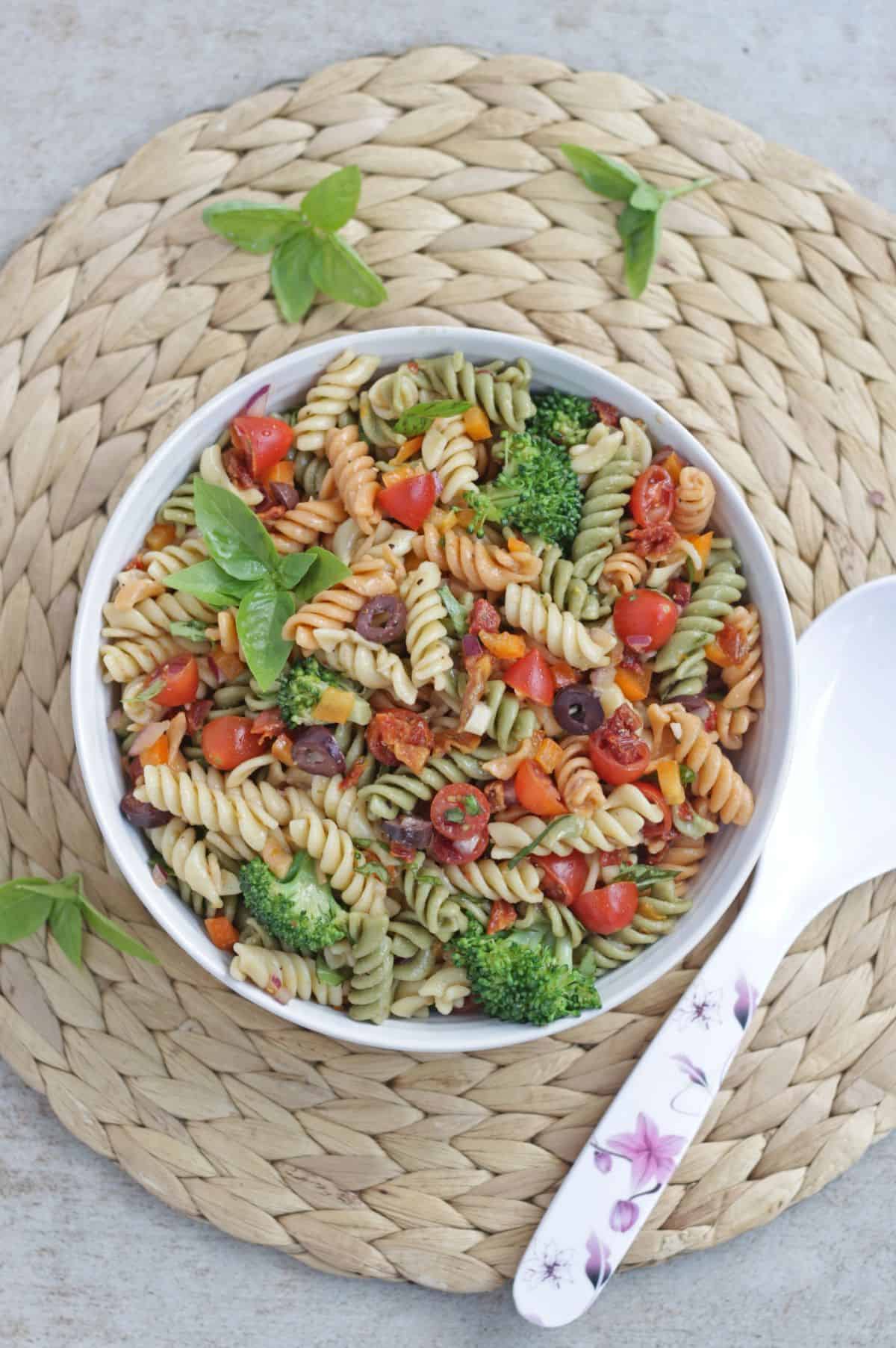 salad with pasta, broccoli, olives and basil in a mat with a serving spoon on side