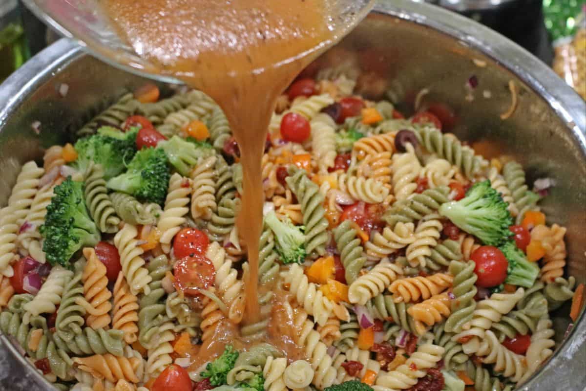 pouring salad dressing in pasta salad