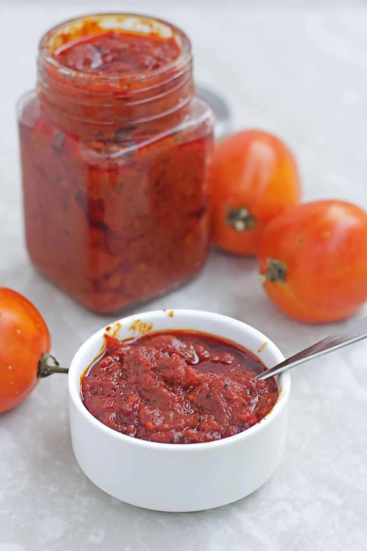 tomato pickle in a bowl with spoon and in a jar with tomatoes in the background.