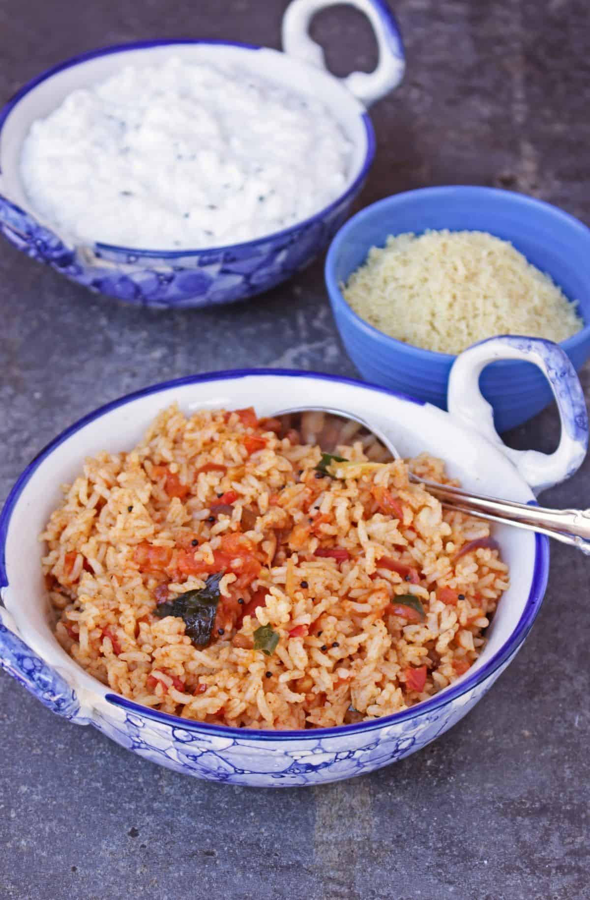 tomato rice ina bowl with spoon with curd rice in the background