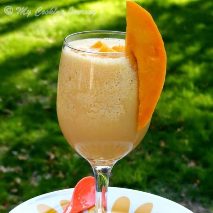 Mango Julius in a tall glass with mango on the side.