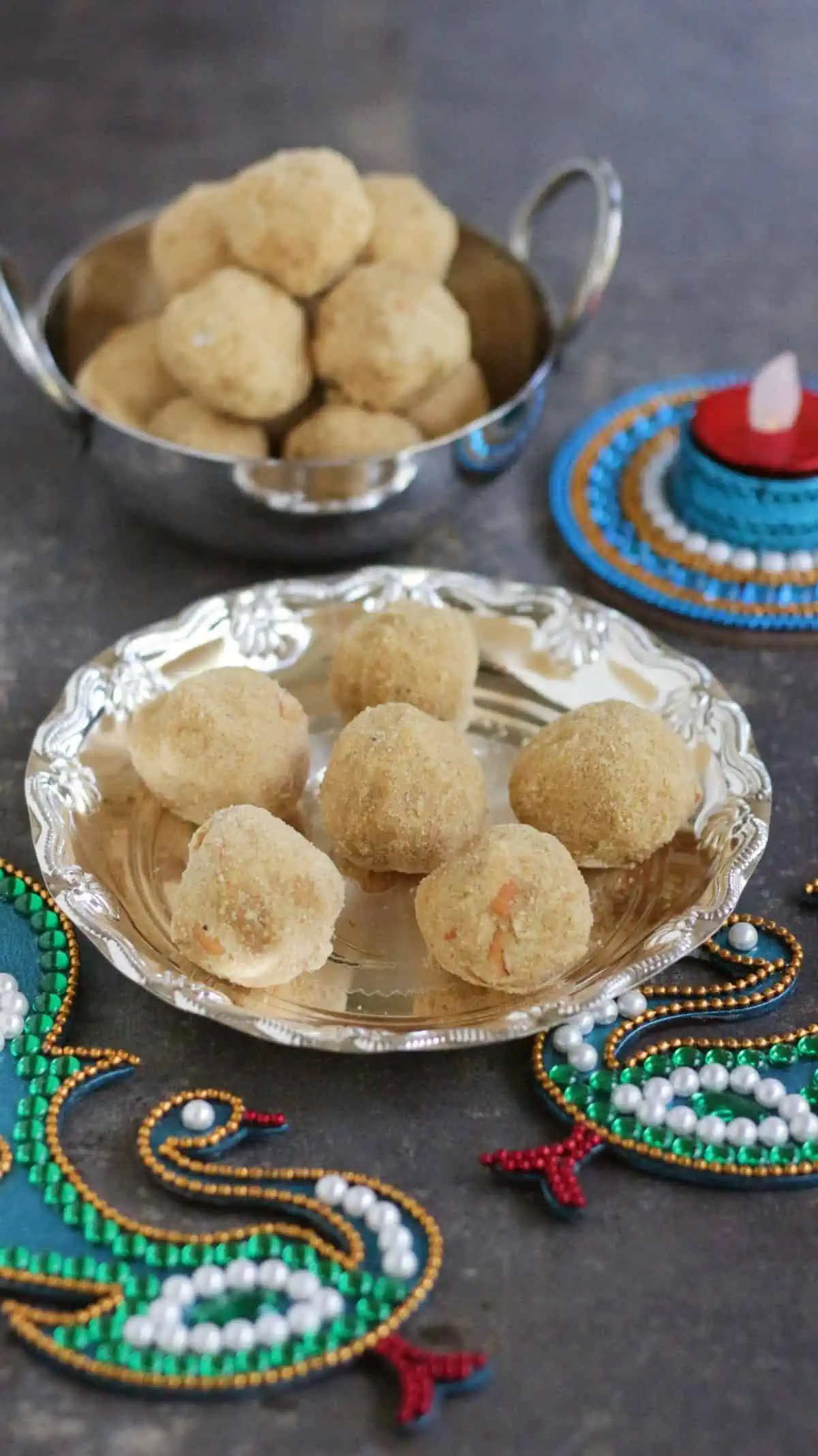moong dal ladoo in a silver plate and more in the background with traditional decorations.
