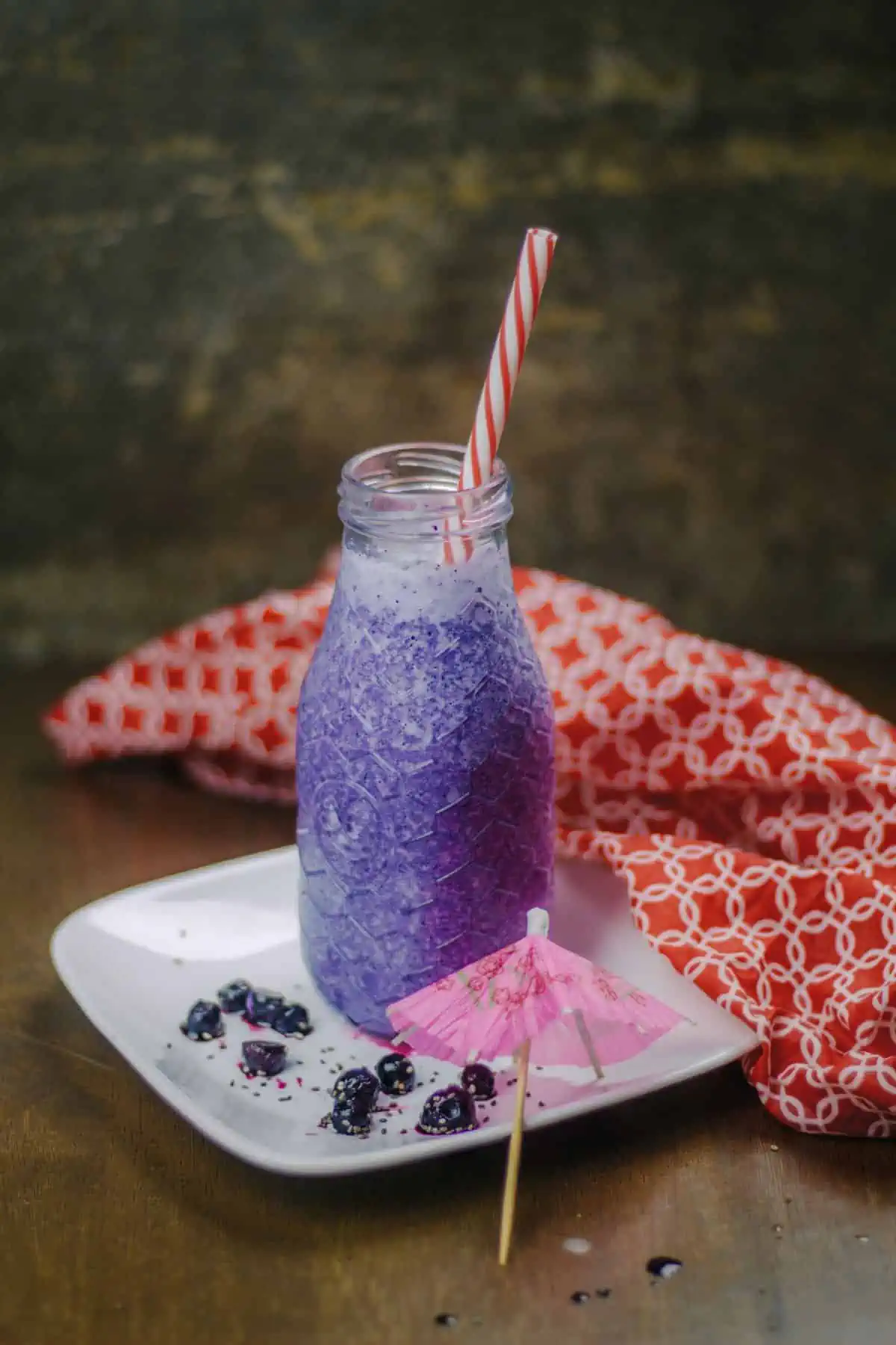 Blueberry smoothie in a glass bottle with straw.