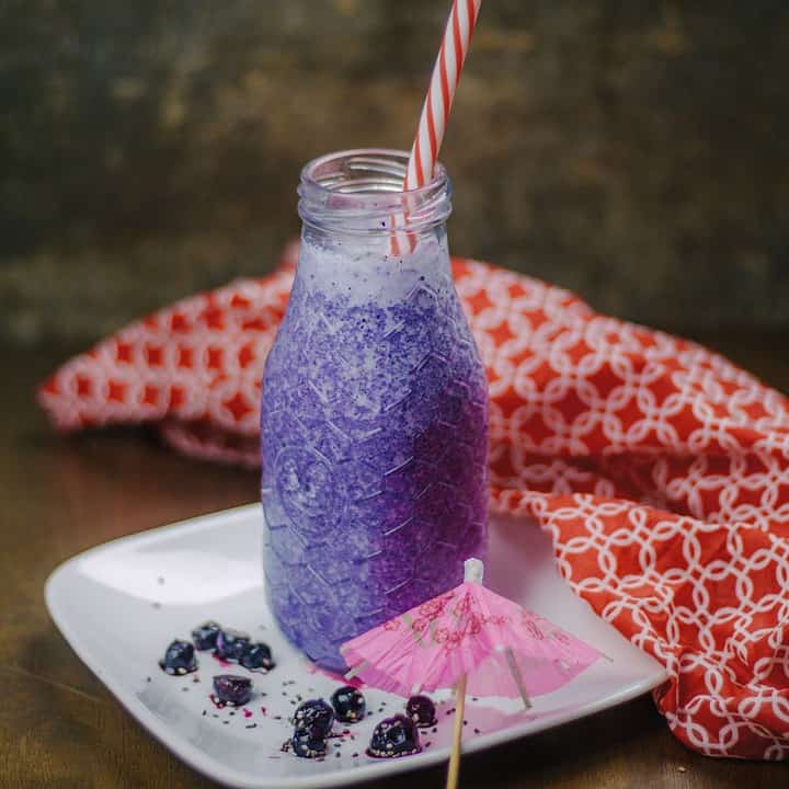 Square image of blueberry banana smoothie in a glass bottle.