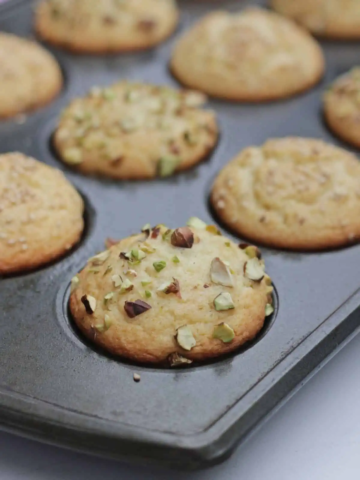 Close up shot of muffin in muffin tin garnished with pistachios.