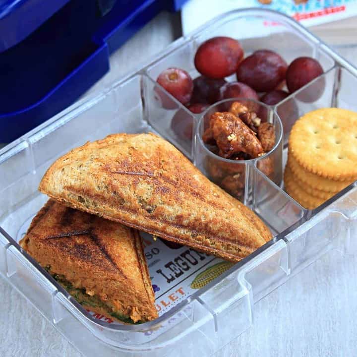 Potato Masala Sandwich in a lunch box with cookies and grapes - Featured Image