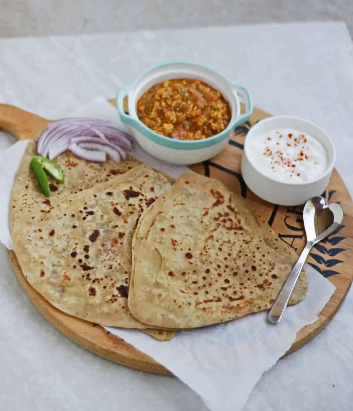 Paratha along with subzi and yogurt and sliced onion and green chilies on a plate.