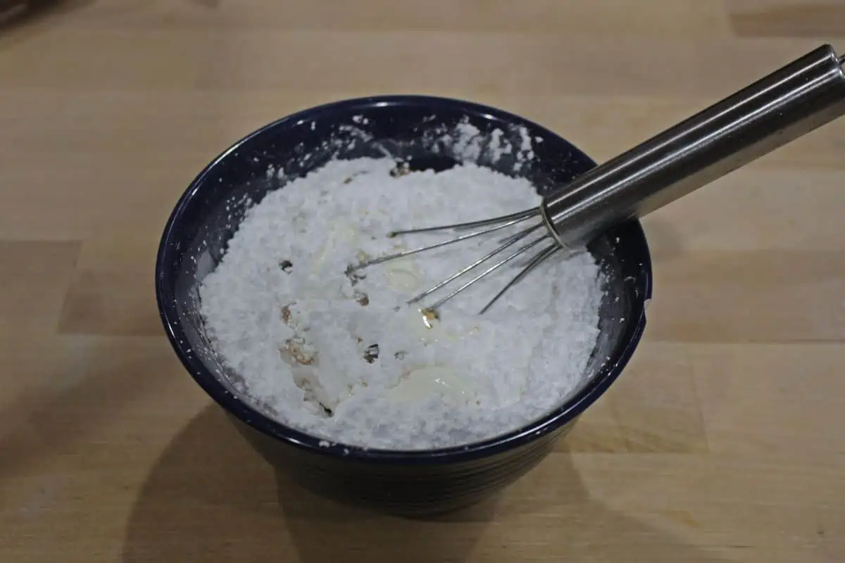 Powdered sugar and vanilla in a bowl with a whisk.