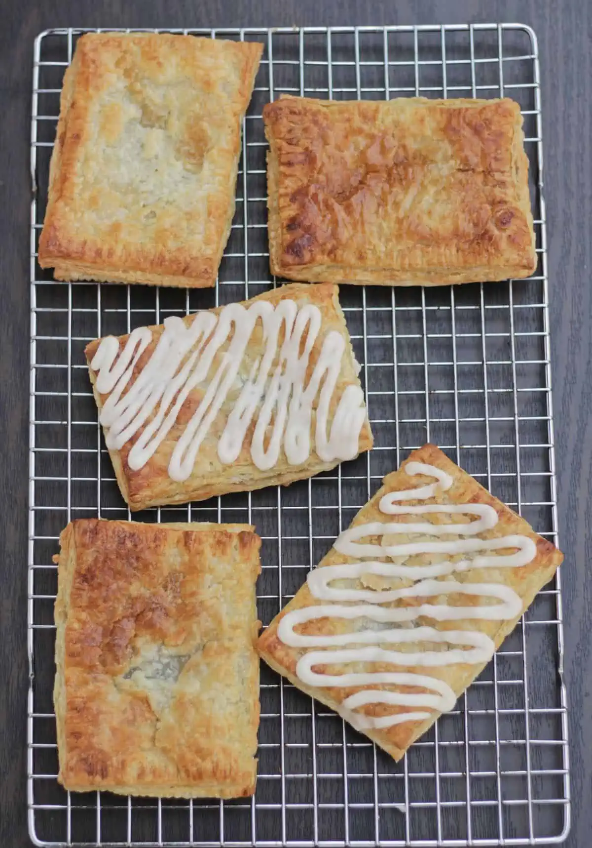 5 toaster strudels with icing drizzle on a rack.